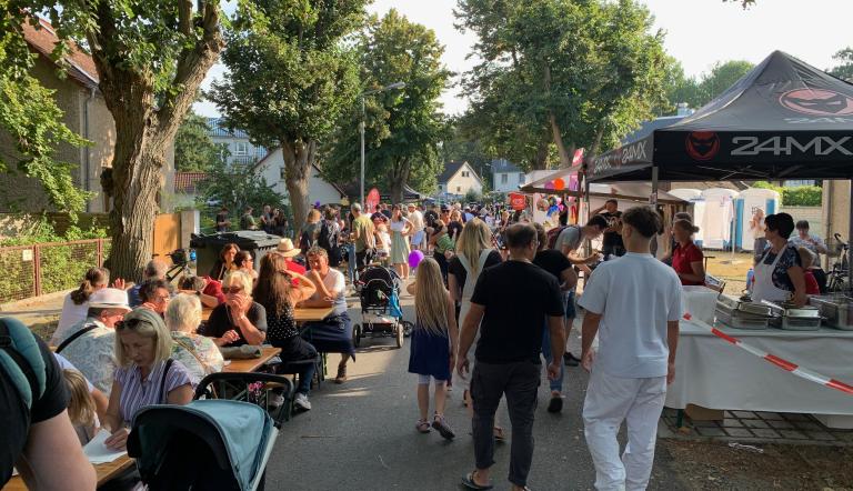 Golmer Dorffest 31.8.2025 Blick in einen der buntern Straßenzüge mit Tischen und Menschen beim Trinken und Essen in Gesprächen