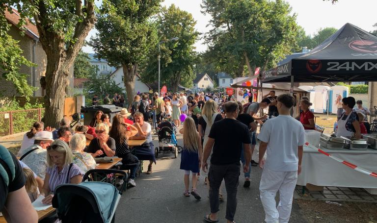 Blick in einen der buntern Straßenzüge mit Tischen und Menschen beim Trinken und Essen in Gesprächen